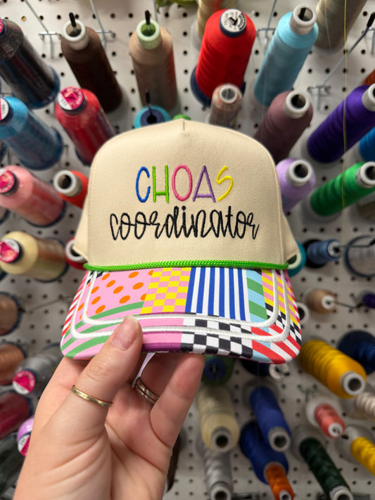 Colorful cap with 'CHAOS COORDINATOR' embroidered in colorful letters displayed in front of spools of thread.